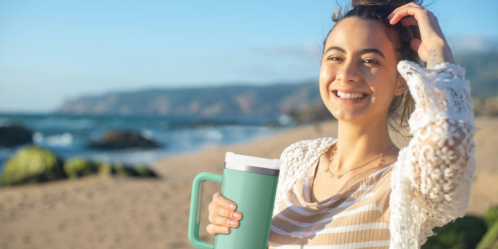 Woman on a beach, smiling holding a teal 40oz tumbler